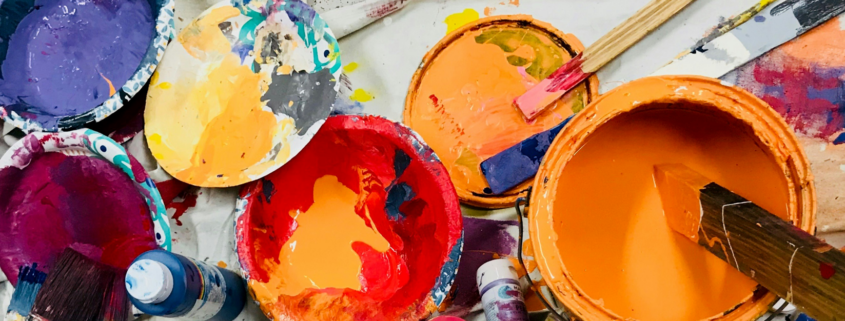 bowls and buckets of paint from orange, purple, pink and yellow on a drop cloth