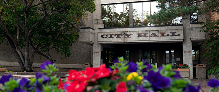 Image of the entrance of Saskatoon's City Hall with colourful flowers in the foreground.