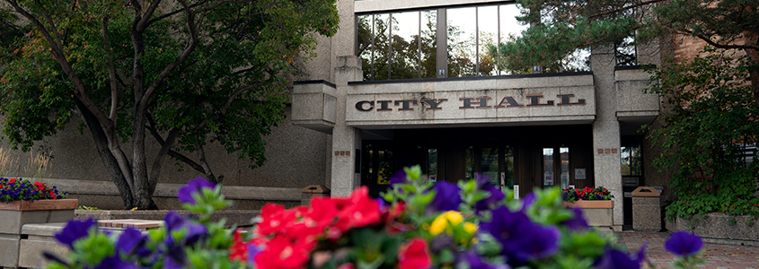 Image of the entrance of Saskatoon's City Hall with colourful flowers in the foreground.
