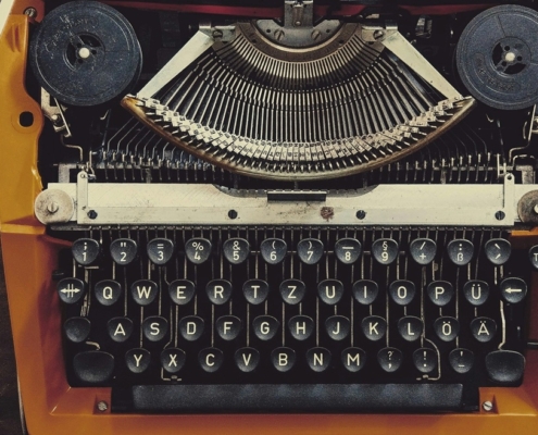 picture of a typewriter, in between a cup of black coffee, a smart phone, and a screenwriting book