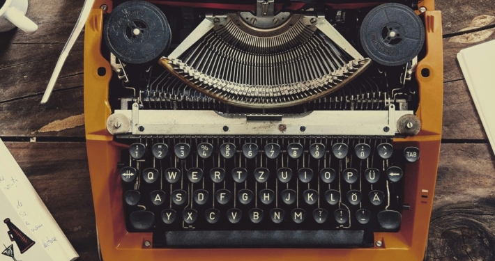 picture of a typewriter, in between a cup of black coffee, a smart phone, and a screenwriting book
