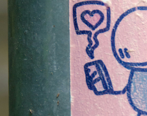 Doodle of person looking at their cellphone with a bubble with a heart at its centre coming from it. The doodle is in blue pen on pink paper.