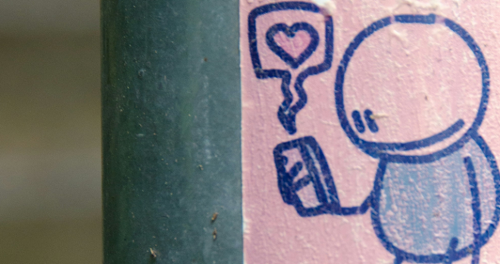 Doodle of person looking at their cellphone with a bubble with a heart at its centre coming from it. The doodle is in blue pen on pink paper.